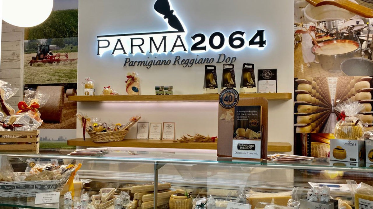 Interno dello spaccio del Caseificio di Fidenza, con il banco frigo e l'insegna luminosa Parma2064
